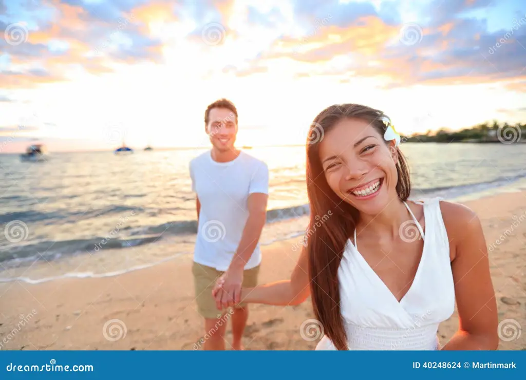 Pasangan yang bergandengan tangan di pantai saat matahari terbenam