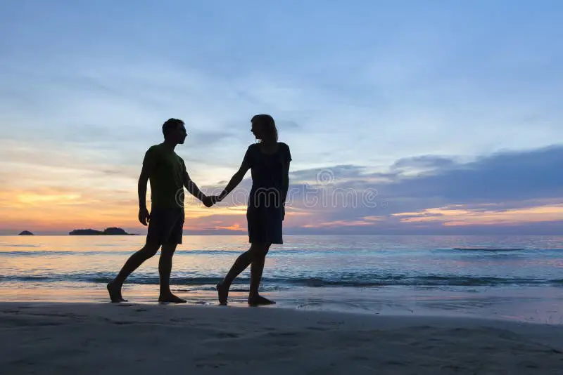 Pasangan bahagia berjalan di pantai saat matahari terbenam