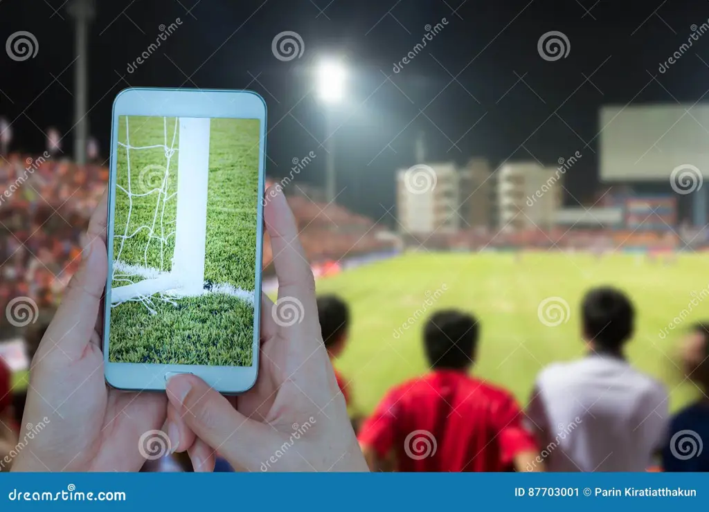 Gambar tangan seseorang memegang smartphone yang menampilkan siaran langsung pertandingan sepak bola