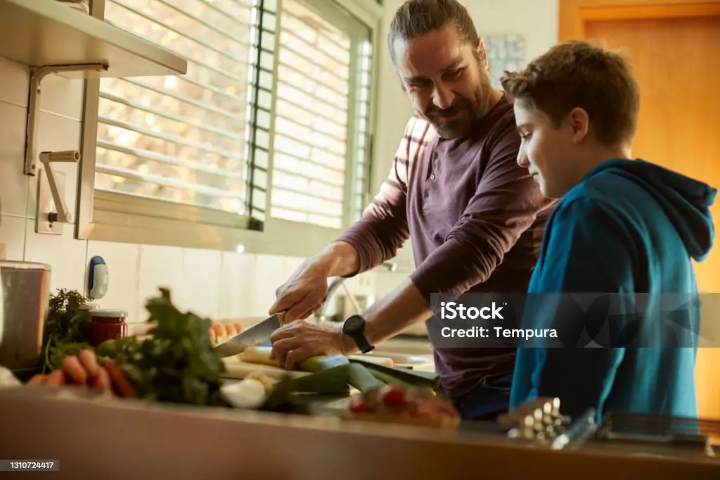 Seorang ayah dan anak laki-lakinya sedang memasak bersama di dapur.